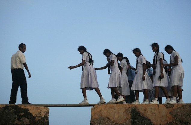 In Sri Lanka, a group of schoolgirls walk across a plank between the walls of the 16th-century Galle fort on July 8, 2009. (SOURCE: takepart.com)